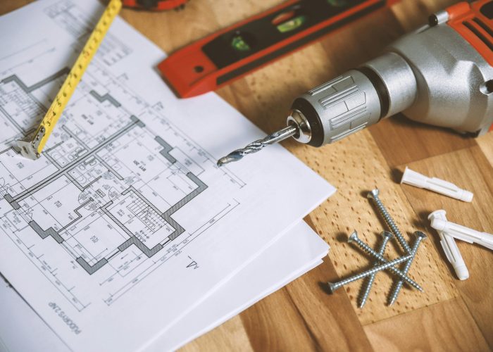 Close-up of construction blueprint with tools like drill and screws on a wooden table.